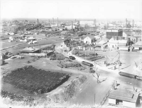 Panoramic view of Golden Mile and Boulder taken from Ivanhoe, large amount of mine timber in foreground, headframes and mine building.  EGHS neg BA.46  TSGM plate 6.1.239 (part).  Taken from Ivanhoe (Drysdale headframe?)  Note Golden ? No. 3 headframe between distant chimneys.Gt Boulder mainshaft headframe (centre distance) with ladgerwood? towers for tailings stackings behind.  Golden horseshoe main shaft to right behind Ivanhoes brush water cooler - note timber pile left foreground (firewood).  1905