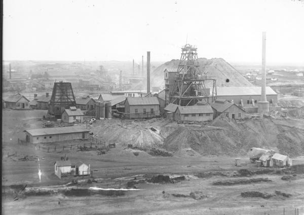 Associated Northern, Iron Duke Shaft, Headframe with accompanying Mine Buildings, chimneys, dumps; Town Buildings in background.