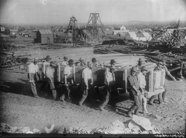 Men carrying first Zinc Boxes in the Goldfields at Lake View Consols also showing headframes, timber piles and assosiated mine buildings.