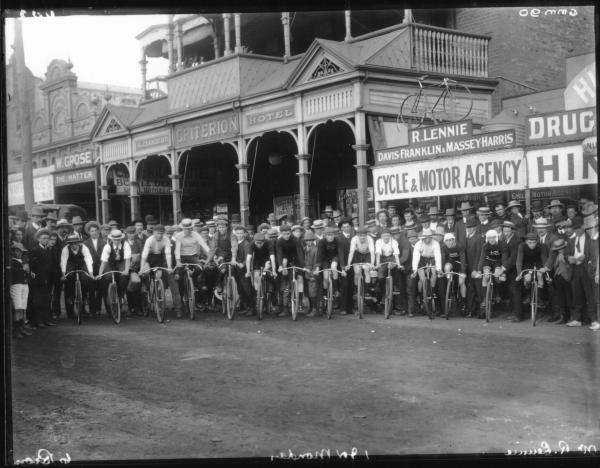 Large group of cyclists in Hannan Street outside Criterion Hotel and Mr. R. Lennie's Cycle Shop.  Large crowd watching start of road race.