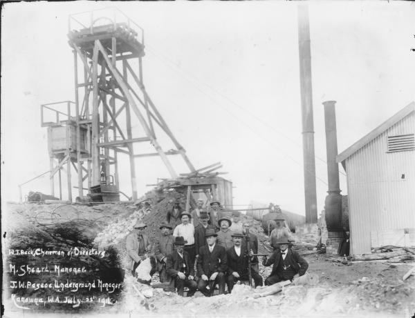 Victoria Gold Mine Kanowna showing wooden headframe and group of men.  Writing on photo 'W.J. Beck, Chairman of Directors, M. Sheard Manager, J.W. Pascoe Underground Manager, Kanowna, W.A., July, 25th, 1916.