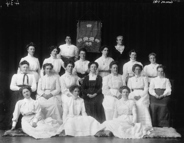 Group Portrait of Womens Christian Temperance Union Group. Mrs Annie Throssell presents banner to local W.C.T Group. Lady 2nd row from back far left: Sister Mildred Fairclough, 'Sister of the People' pioneer nussing sister 1896 trained in Adelaide.  Lady in centre in dark dress: Mrs Annie Throssell wife of George Throosell MLA & Comm of lands and who was sympathetic to womens causes.  Lady to right of Mrs Throssell Mrs R Hamilton wife of Richard Hamilton manager of Great Boulder Mine.  L:ady seated in...