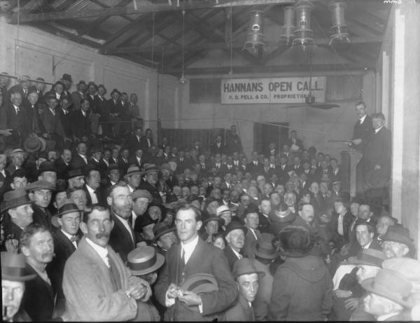 Large crowd of men at Hannans Open Call, Kerosene Heaters hanging from roof, Proprietor H.D. Pell & Co.