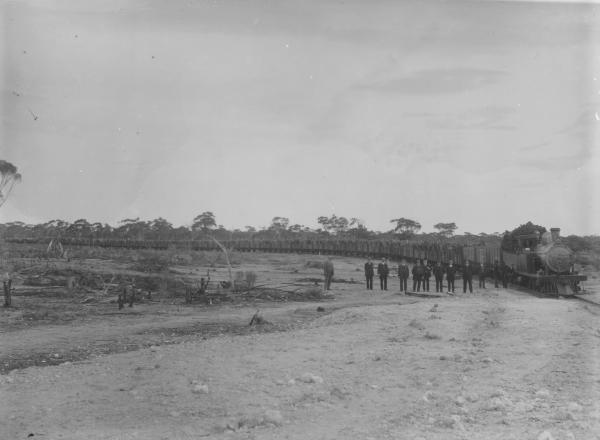 Kurrawang**? see below Firewood Co. Woodline Train at Kurrawang pulling Wagons loaded with wood.  Group of men standing near Train.  S.A. Premier and party.NOTE:' Locoo 'Ivanhoe' an O class 2-8-0 type loco, #219 purchased from the WA Government Railways in October 1908 by the ** WA Goldfields Firewood Supply Ltd for hauling firewood trains into Kurrawang.  Named IVANHOE by the company, later numbered #1 (about 1924)' - SOURCE- Mr Adrian Gunzburg, 9 Foster Ave, Glenhuntly, Vic 3163 (14/8/95)