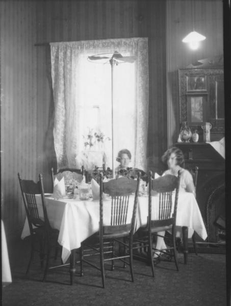 Two women sitting at dinner table in dining room, fan in middle of table. (Reeves)