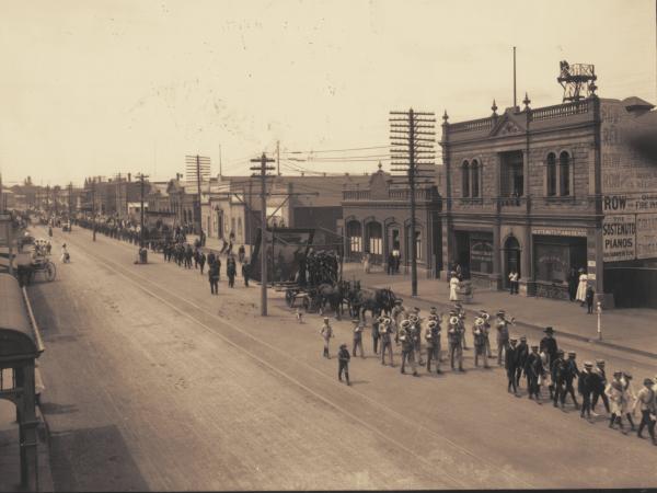 St Patrick's Day Parade in Burt Street. Procession with trade union banners, brass bandd and horses pulling jinkers. Boulder Fire Station on left and Friendly Societies building. Sostenuto Pianos.