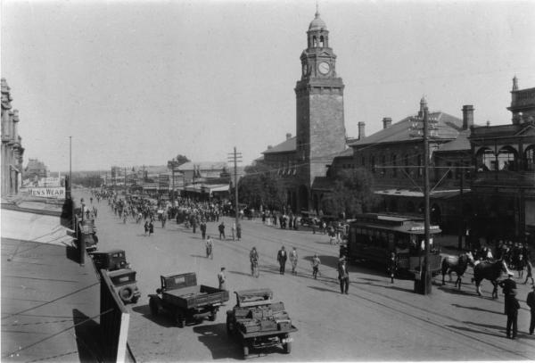 Hannan St, viewed from Maritana St., Many people and cars coming up street, tram, horses, cars and bicycles in street. 1908