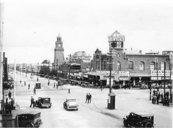 Intersection of Hannan and Maritana Streets looking towards the post office.  Shows the Mechanics Institute and McKenzie Building.  Shows lots of motor vehicles and people standing on street corners.