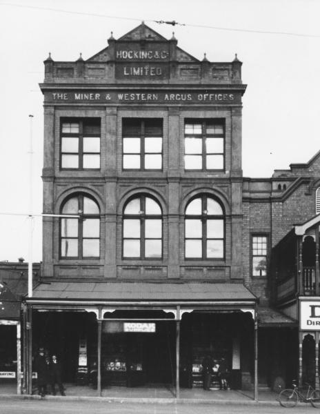 Hocking & Co building (Kalgoorlie Miner) Hannan Streeet, Kalgoorlie.  Shows part of Exchange Hotel on right.  Few men and boys standing outside.