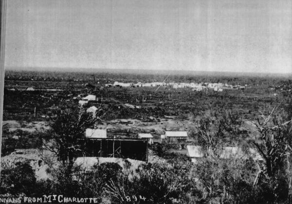 'Hannans from Maritana Hill'. Mining in progress in foreground with tents among dumps and sparce vegetation. Some more subtantial housing in background.