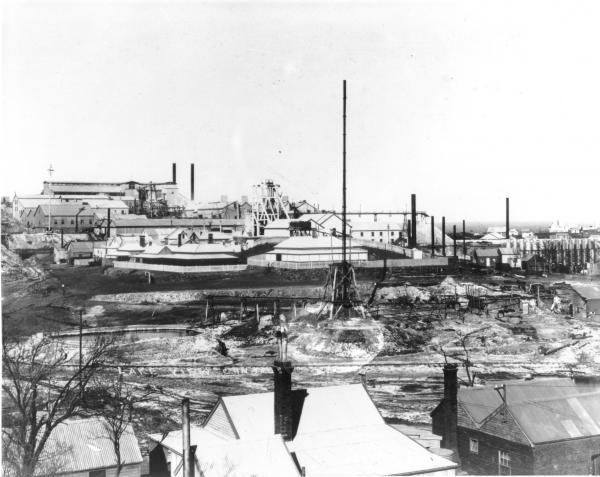 'Lake View Consuls'- corrugated iron rooms with brick chimneys in foregroundfenced from dry settling ponds, extensive mine buildings in background.