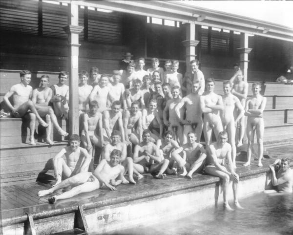 Group of naked men/boys posed on seats of stand by Kalgoorlie's first swimming pool in Victoria Park.