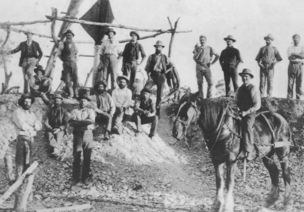 Slug Hill Grand Junction Mine about 1898. Group of 17 miners beside wooden frame and windsail, ore bucket, horse in full harness on right  Donated by Jessie Gray in 1989. Photo by Rembrant Photo Co.