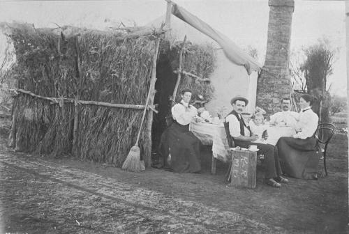 Traditional homestead, smartly dressed family enjoying dinner around table B/W.