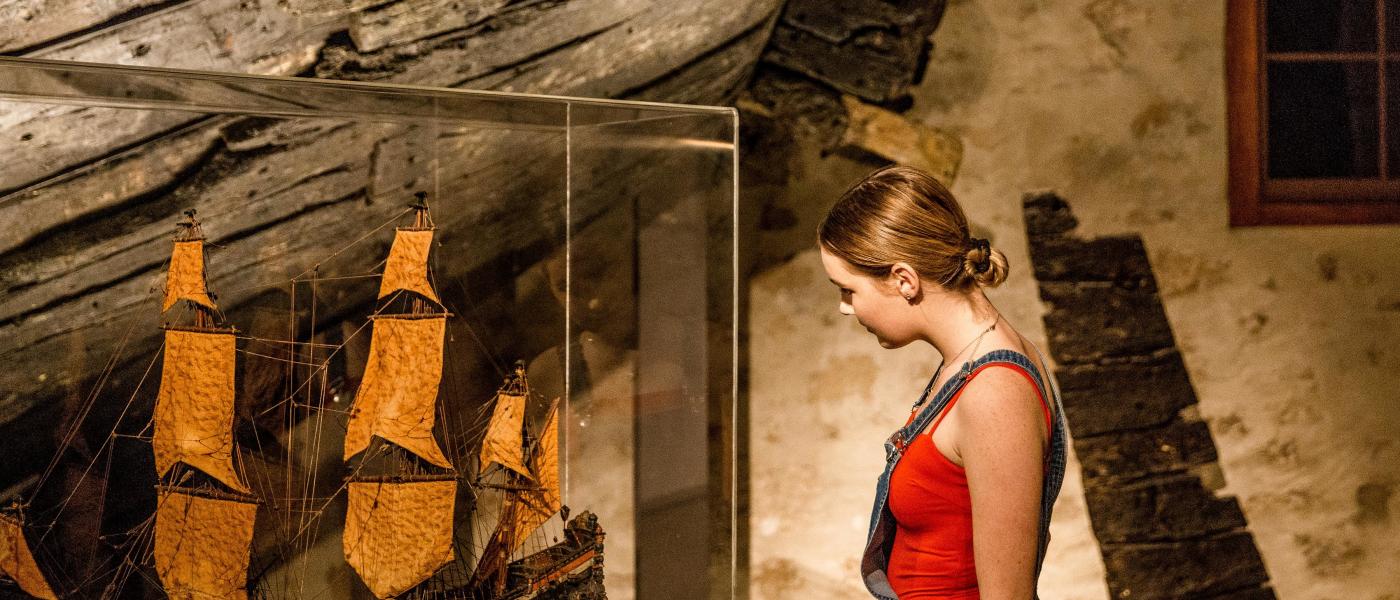 A woman standing in a Museum gallery examines a model ship in a showcase