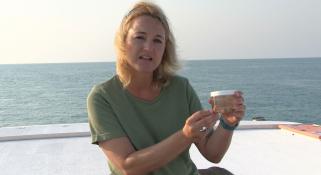 Monika Schlacher-Hoenlinger holding a jar containing soft coral, sitting on the back of a boat