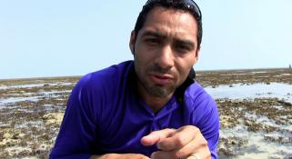 Oliver Gomez talking to camera, crouched down on a reef
