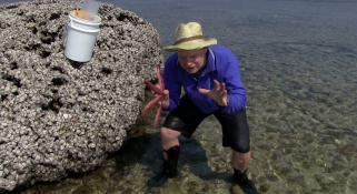 Merrick Ekins holding a sea star, crouching up to his ankles in water on a reef