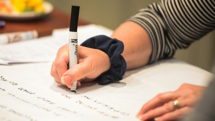 A woman's hand holding a pen writing on a large piece of paper.