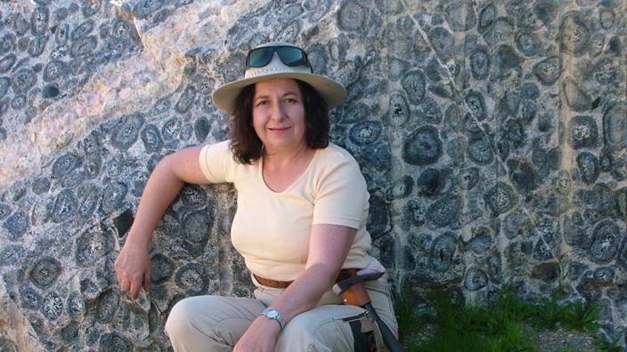 A lady standing in front of a rock wall filled with circular rock formations