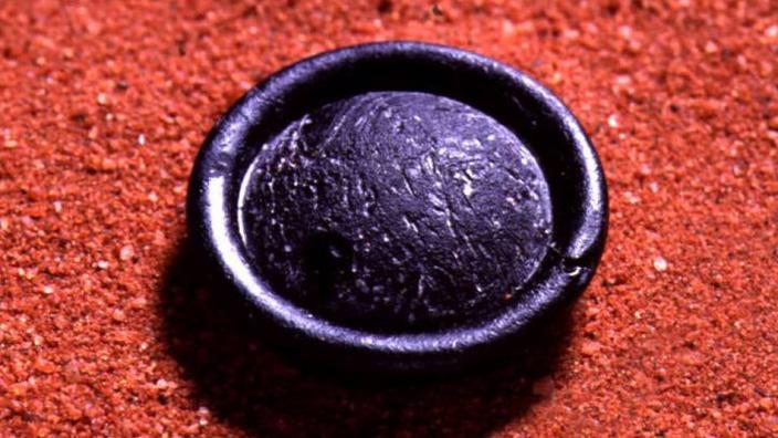 A round black tektite on red soil background
