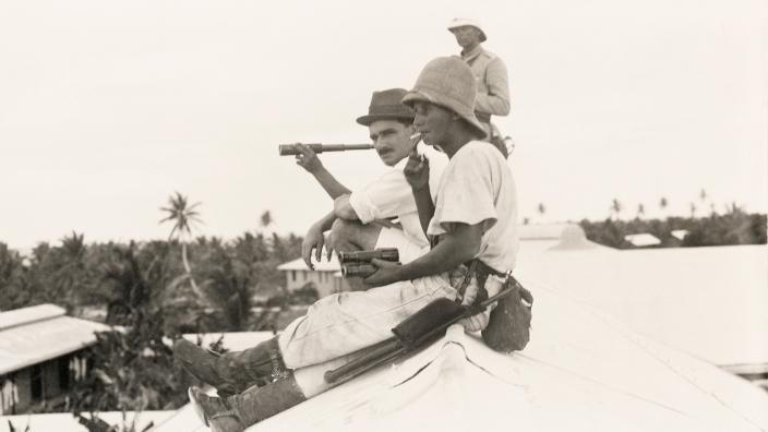 Two people sitting on a roof top watching a naval battle