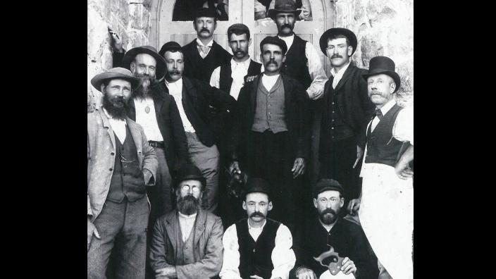A group of builders wearing 19th century style clothing standing in front of a court house