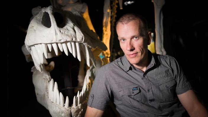 A scientist standing next to a T-Rex skull