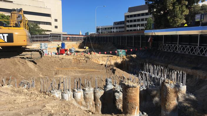 A construction site with a large hole in the ground revealing concrete poles