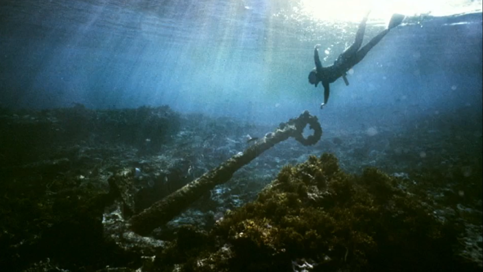 A snorkeler dives towards an anchor deep in the ocean.