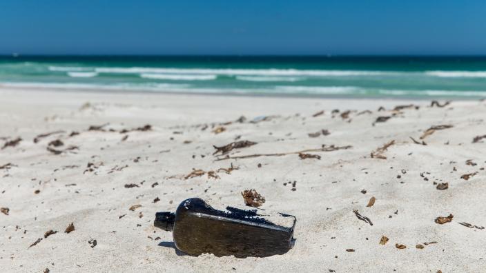 "The bottle is half submerged in sand in the foreground, with crashing waves in the background."