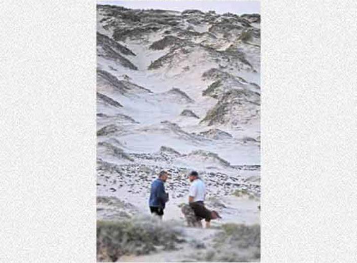 Two people standing below a large sand dune.