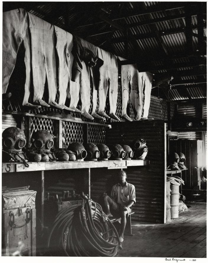 A man sitting in a shed surrounded by pearling and diving gear. 