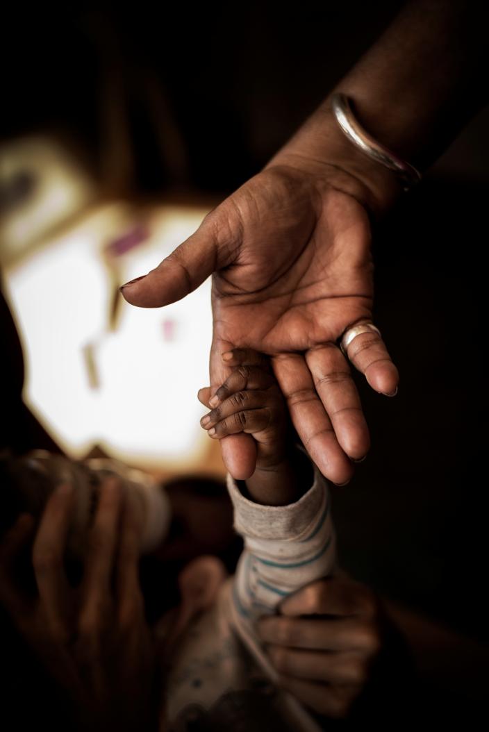 An infant clasping her mother's finger