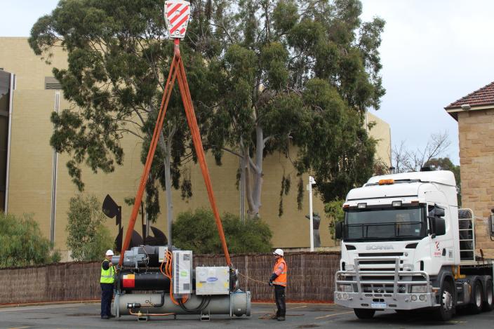 Two workers holding the straps around a large chiller.  The chiller is about to 