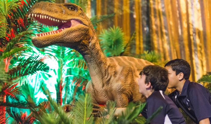 "Two boys looking in awe at a ferocious dinosaur."