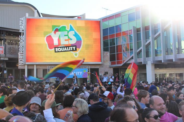 People celebrate the Yes vote, waving LGBQTI flags and a large screen in the background has YES displayed