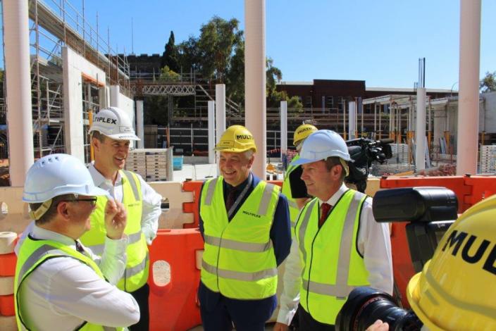 Four men in hard hats and hi-vis vests stand in discussion at the New Museum site.