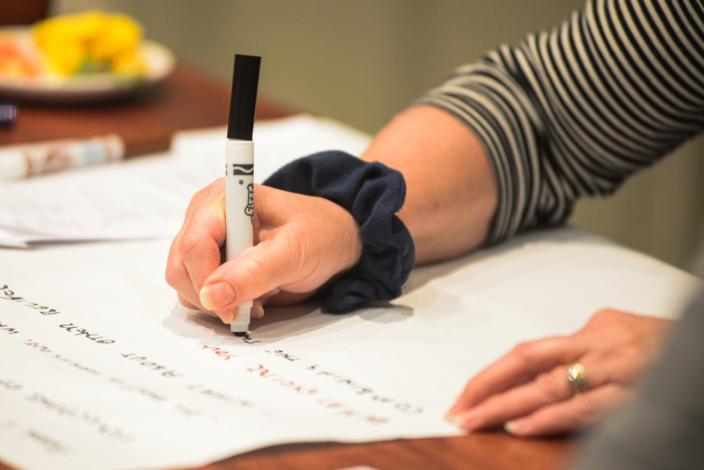 A woman's hand holding a pen writing on a large piece of paper.