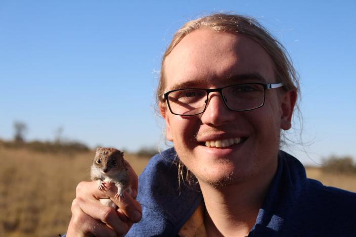 Cameron Dodd wears black glasses and holds a small marsupial in their hand.