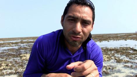 Oliver Gomez talking to camera, crouched down on a reef