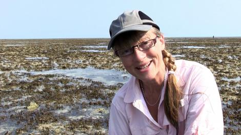 Sue Morrison crouched down on a reef talking to the camera