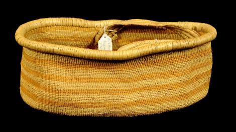 An open, oval shaped, single handled basket with yellow vegetable dye stripes.
