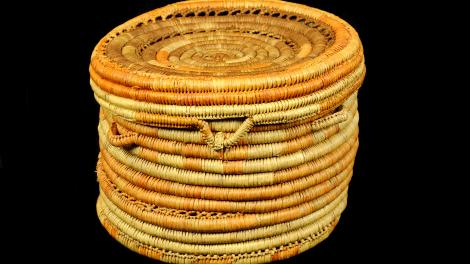 A round, yellow and orange, coiled basket with a lid but no handle. 