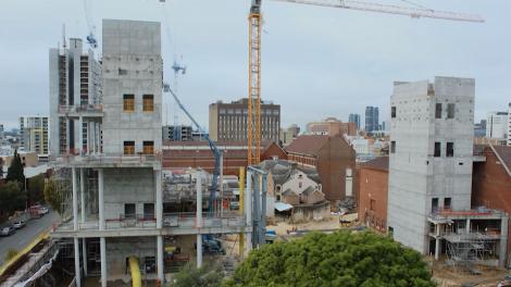 'View of a construction site with two tall thin concrete towers and a yellow crane in between them.'