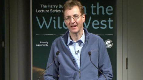 Mark Harvey standing at a podium giving a Lecture