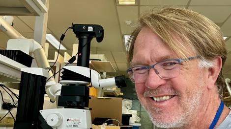 Peter Middelfart wears a light blue shirt and smiles next to a microscope