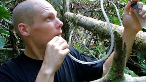 Nikolai Tatarnic holds up a piece of rubber piping and stands in a leafy forrest