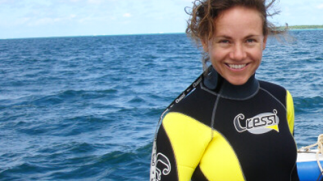 "A woman wearing scuba clothes standing on a boat, in front of the ocean."
