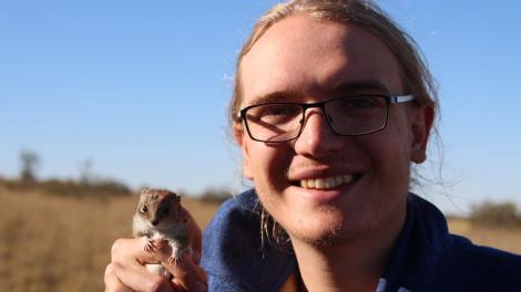 Cameron Dodd wears black glasses and holds a small marsupial in their hand.